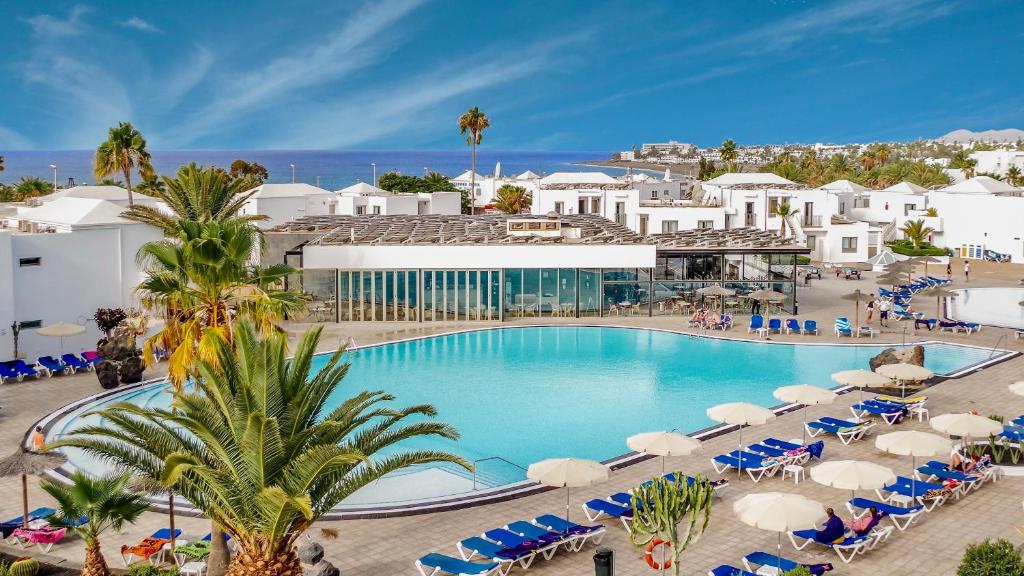 einen Pool mit Stühlen und Sonnenschirmen in einem Resort in der Unterkunft Hotel Floresta in Puerto del Carmen