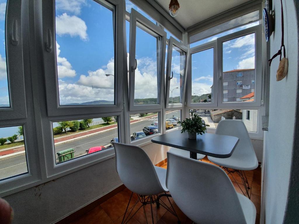 una mesa y sillas en una habitación con ventanas en Muxía Apartamento Malecón enfrente al puerto 4 personas, en Muxía