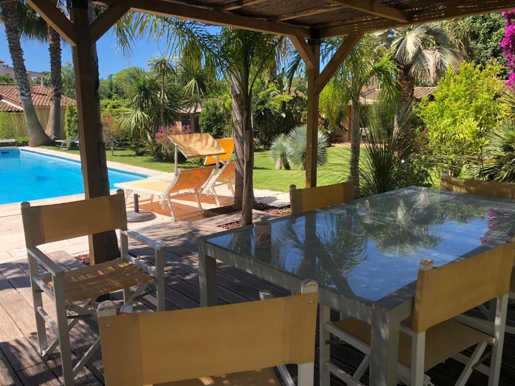 un patio con mesa de cristal y sillas junto a una piscina en Les deux mas, en Bormes-les-Mimosas