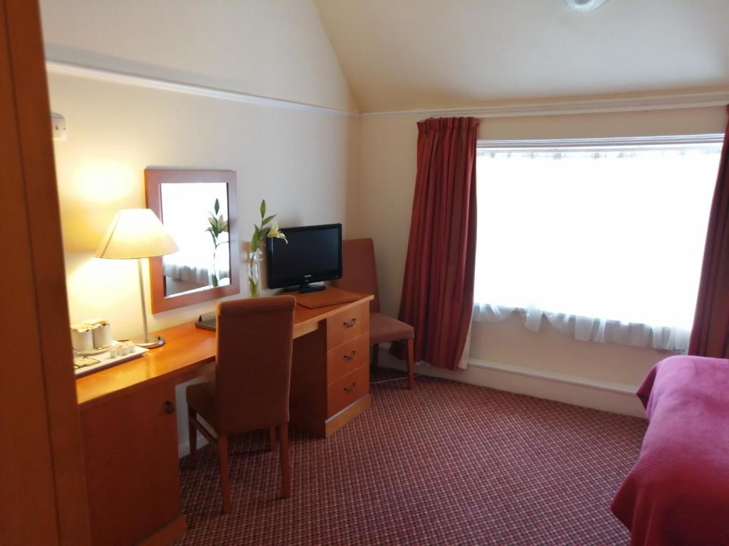 a hotel room with a desk with a computer and a window at The Tudor Hotel in Harrow