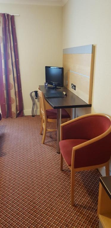 a room with a desk with a computer and chairs at The Tudor Hotel in Harrow