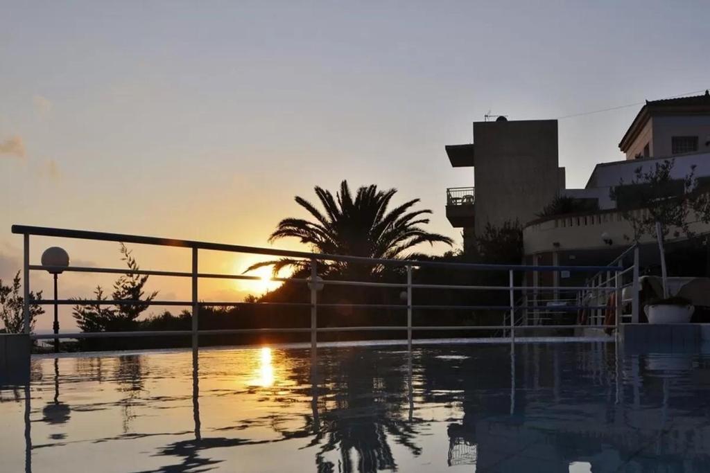 a sunset over a pool with a fence and a palm tree at Pelagia Bay Hotel in Agia Pelagia