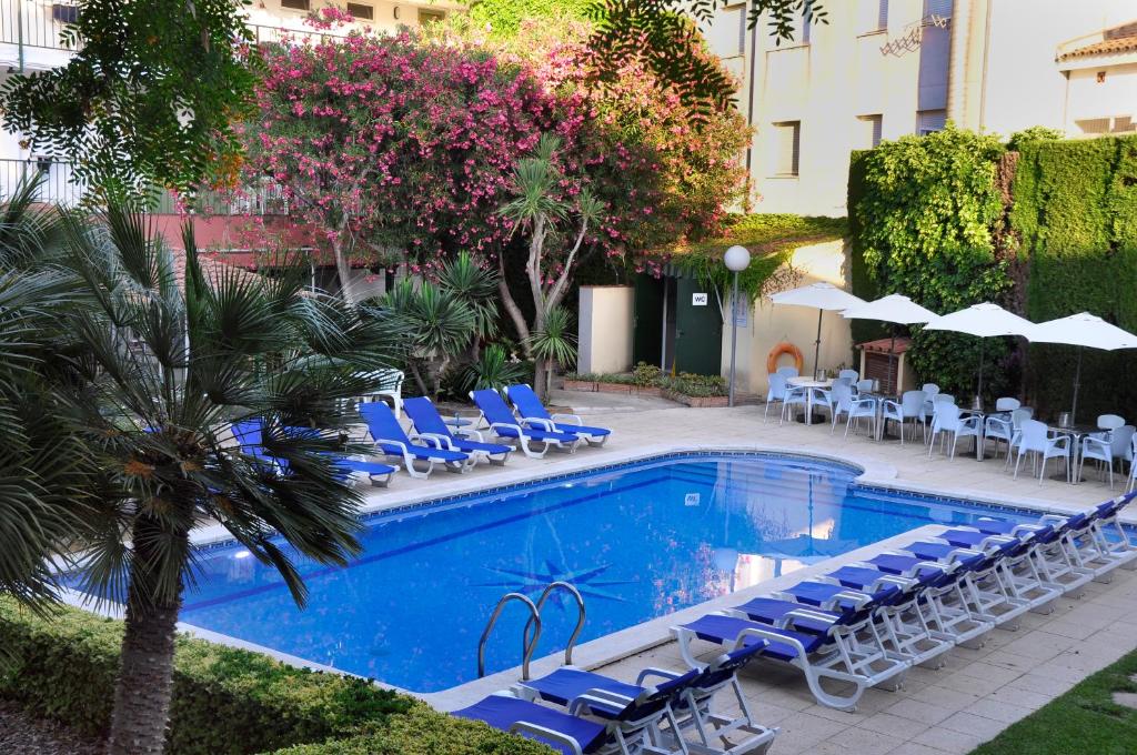 una piscina con tumbonas y sombrillas azules en Hotel Yola, en Altafulla