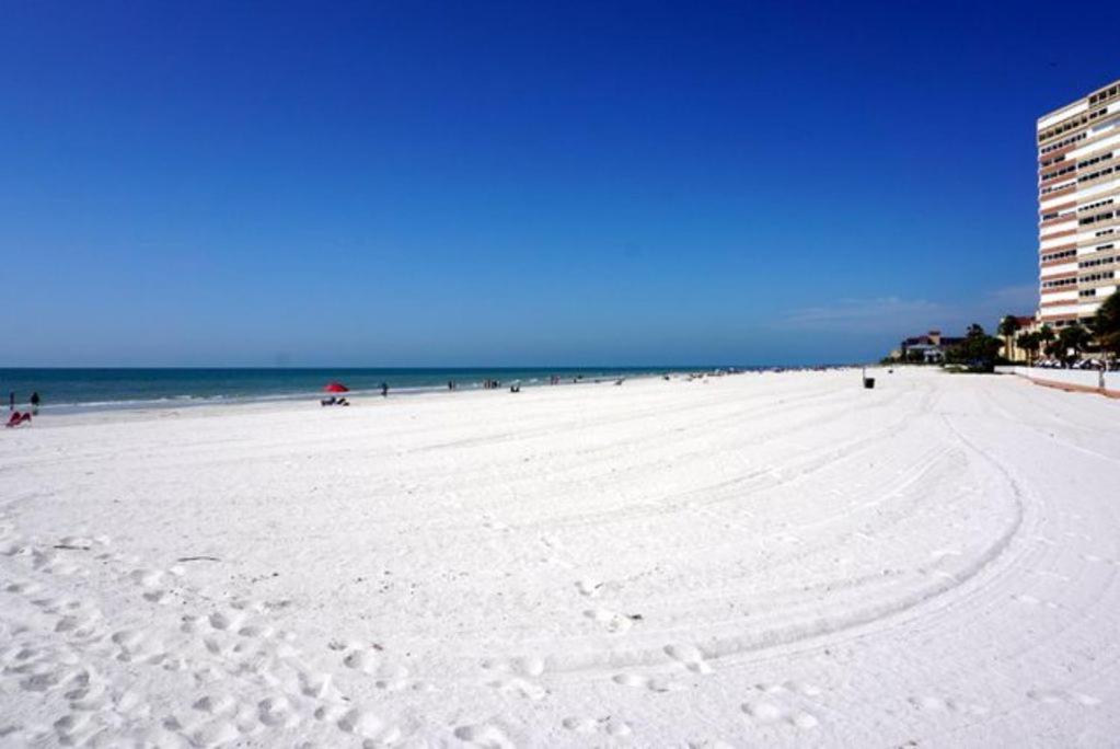 a white beach with people in the water and a building at The Monterey Beach Resort in St Pete Beach