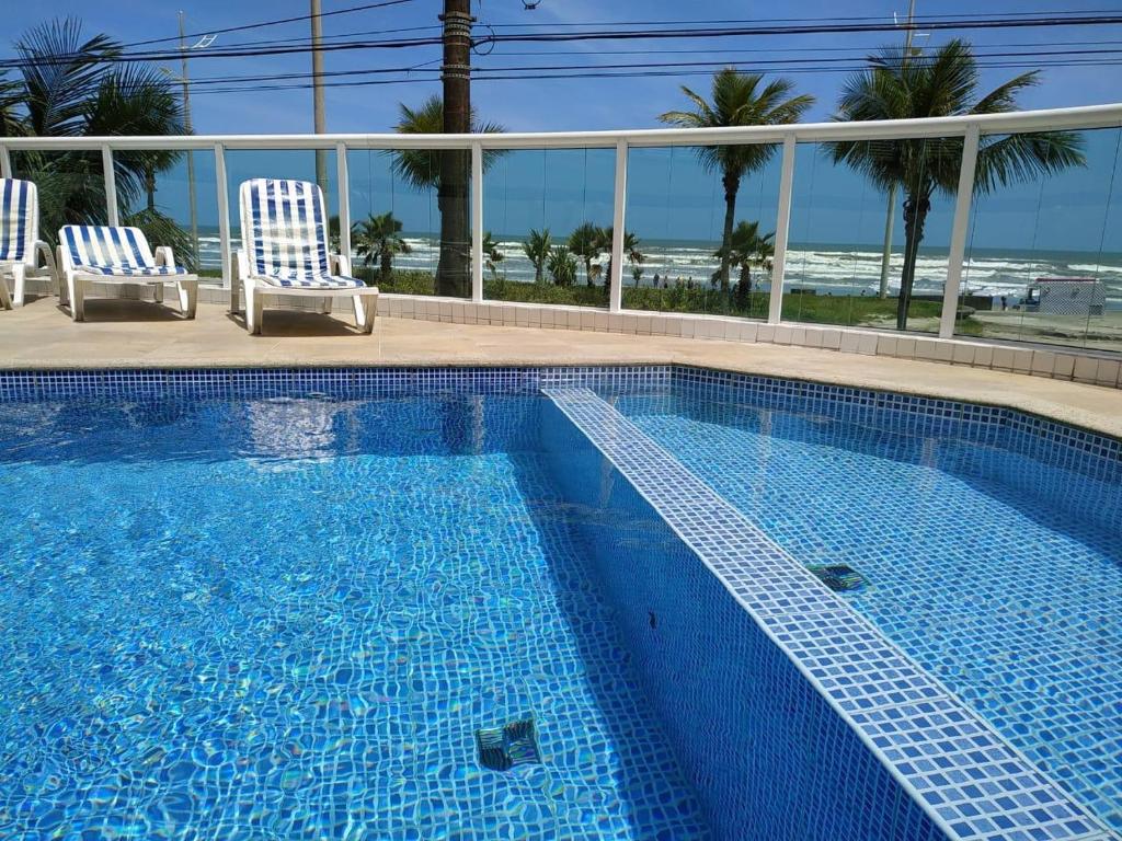 une piscine avec deux chaises et l'océan dans l'établissement Amor e aconchego beira mar e ar condicionado, à Praia Grande