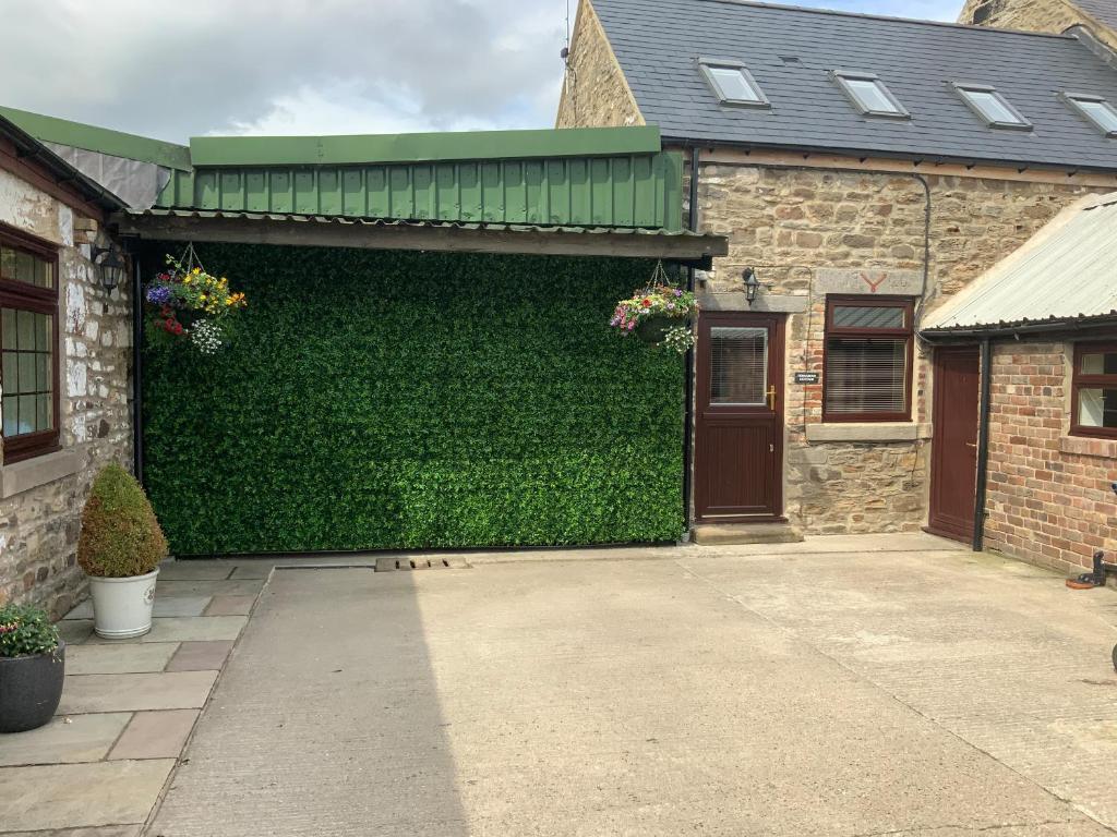 a building with a green hedge in front of a garage at Ferngrove Cottage in Bishop Auckland
