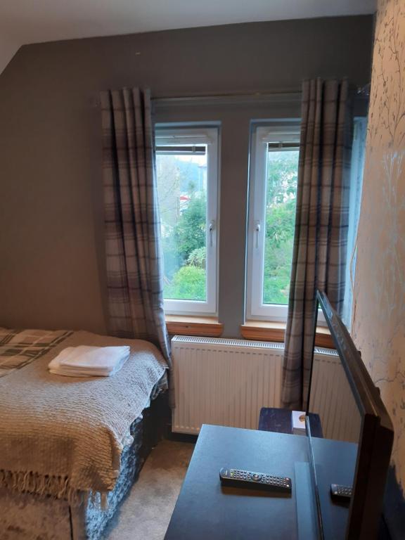 a small bedroom with a bed and two windows at Ardgowan Cottage in Brodick