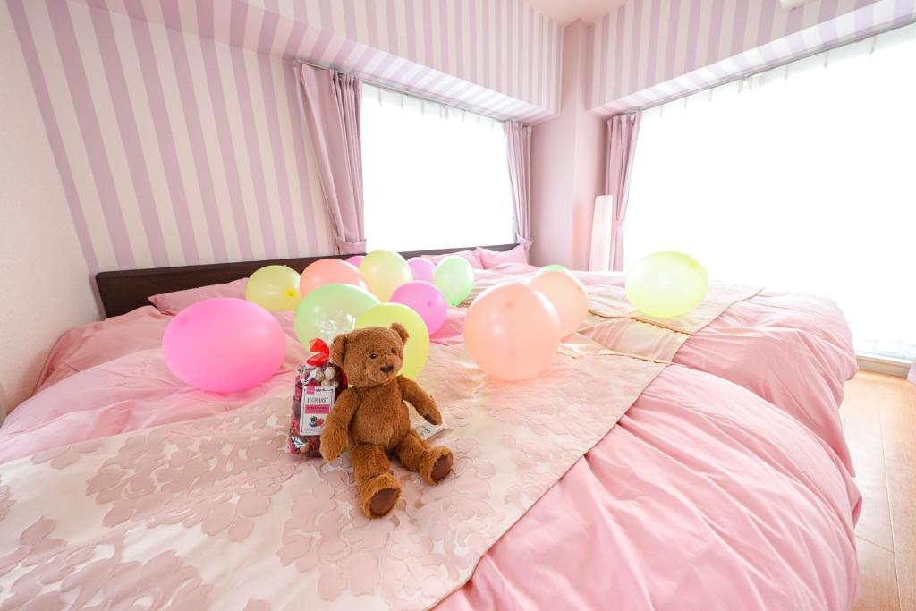 un oso de peluche sentado en una cama con globos en Du Etowaaru, en Nagoya