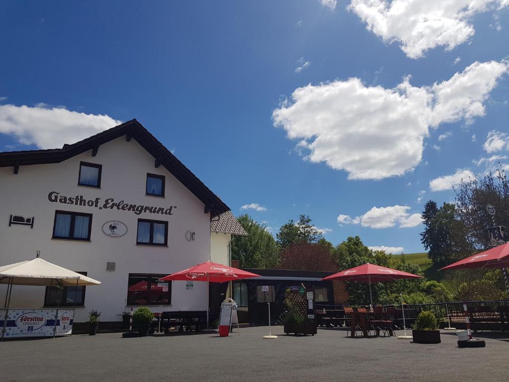 une femme debout devant un bâtiment avec des parapluies dans l'établissement Gasthof & Pension Erlengrund, à Gersfeld