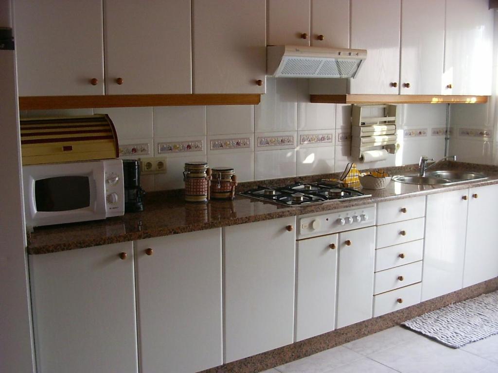 La cuisine est équipée de placards blancs et d'un four micro-ondes. dans l'établissement Apartamento O Grove, à O Grove