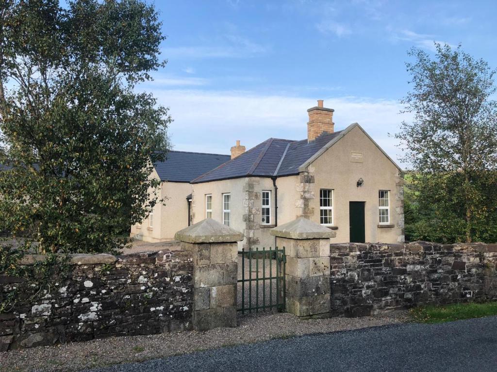 una casa bianca dietro una recinzione di pietra con un cancello di Grannan School, Trillick, Fermanagh and Omagh, Tyrone a Trillick