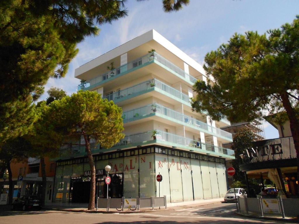 un edificio alto y blanco con árboles delante en Appartamenti Fiore, en Lignano Sabbiadoro