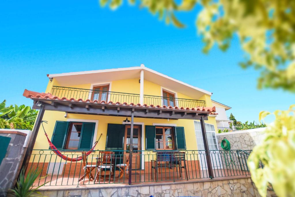 uma casa amarela com uma varanda com mesas e cadeiras em House near CR7 Museum no Funchal