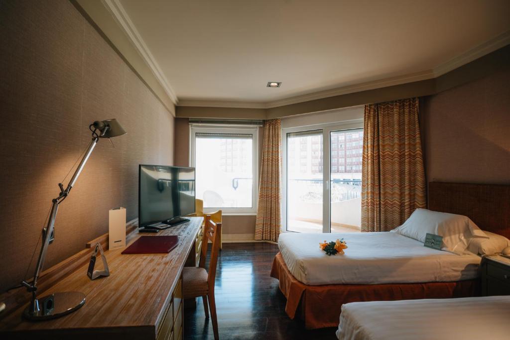 a hotel room with two beds and a desk and a television at Hotel Playa Victoria in Cádiz