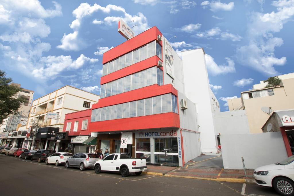 un edificio rojo con coches estacionados frente a él en Hotel Condá, en Chapecó