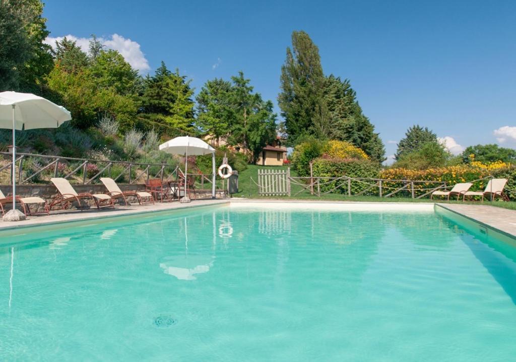 Una gran piscina azul con sillas y sombrillas. en Villa La Ginestra con piscina privata, en Umbertide