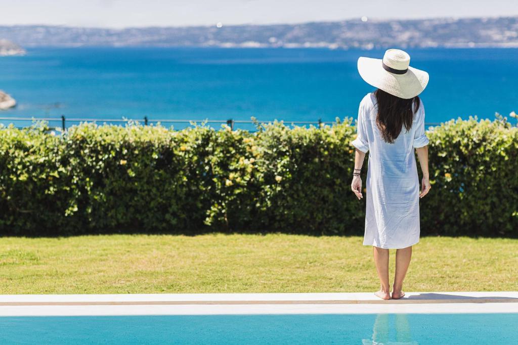 a woman in a white dress and hat standing next to a pool at Miraida Exclusive Residence, a SeaView Sanctuary, By ThinkVilla in Almirida