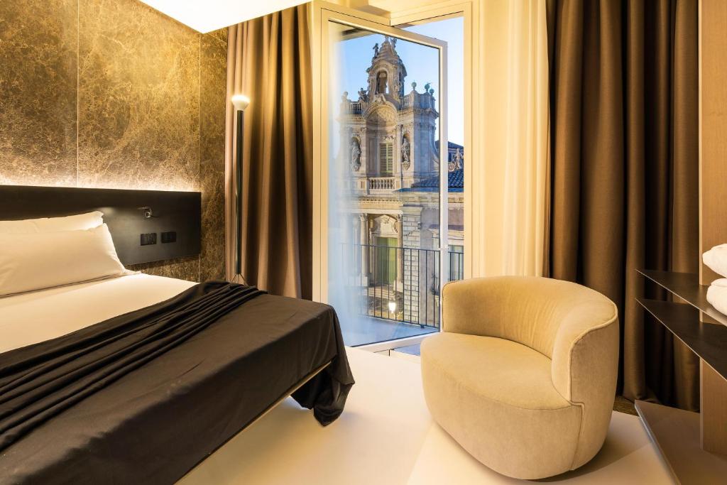 a bedroom with a bed and a chair and a window at Meo Design Suites & Spa in Catania