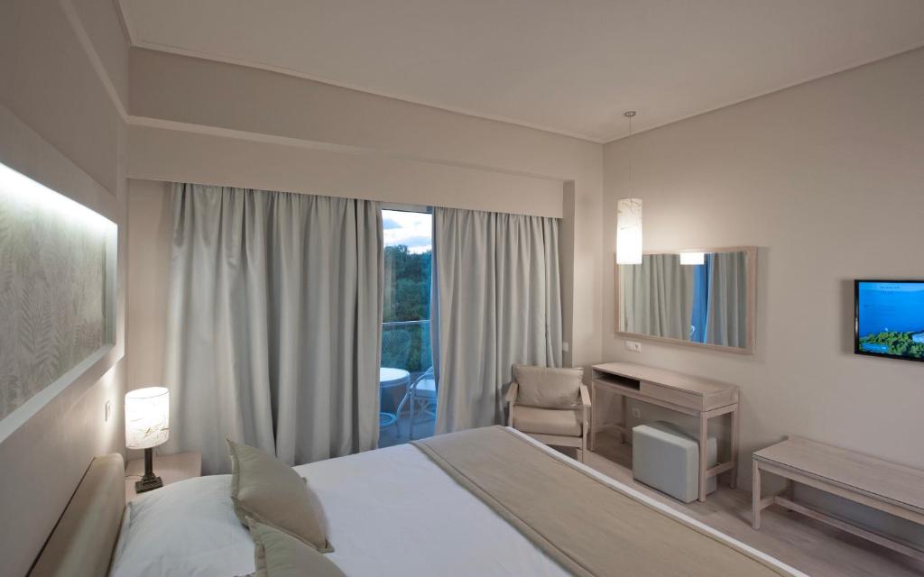 a hotel room with a bed and a desk and a window at Hotel King Saron Club Marmara in Isthmia