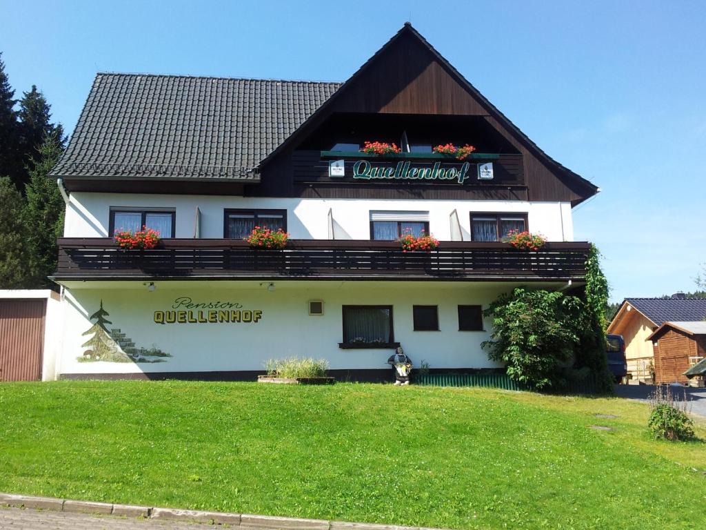 a white house with a black roof and a green yard at Quellenhof Altenau in Altenau