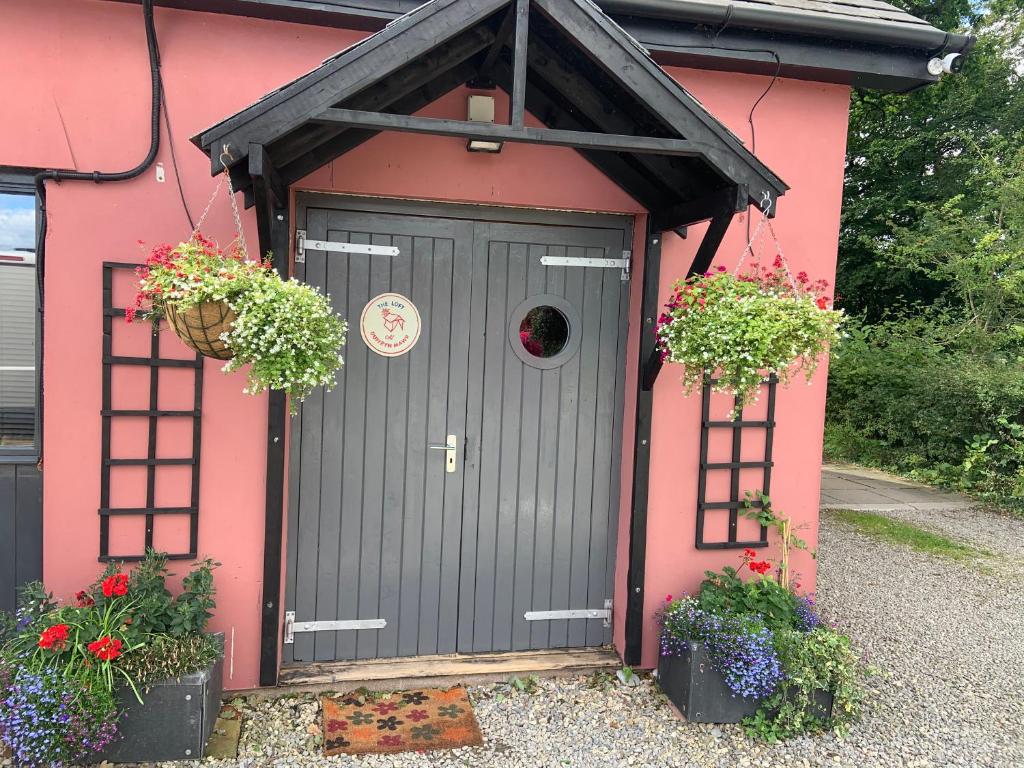 uma casa cor-de-rosa com uma porta cinzenta e duas plantas em The Loft at Duffryn Mawr Self Catering Cottages em Hensol