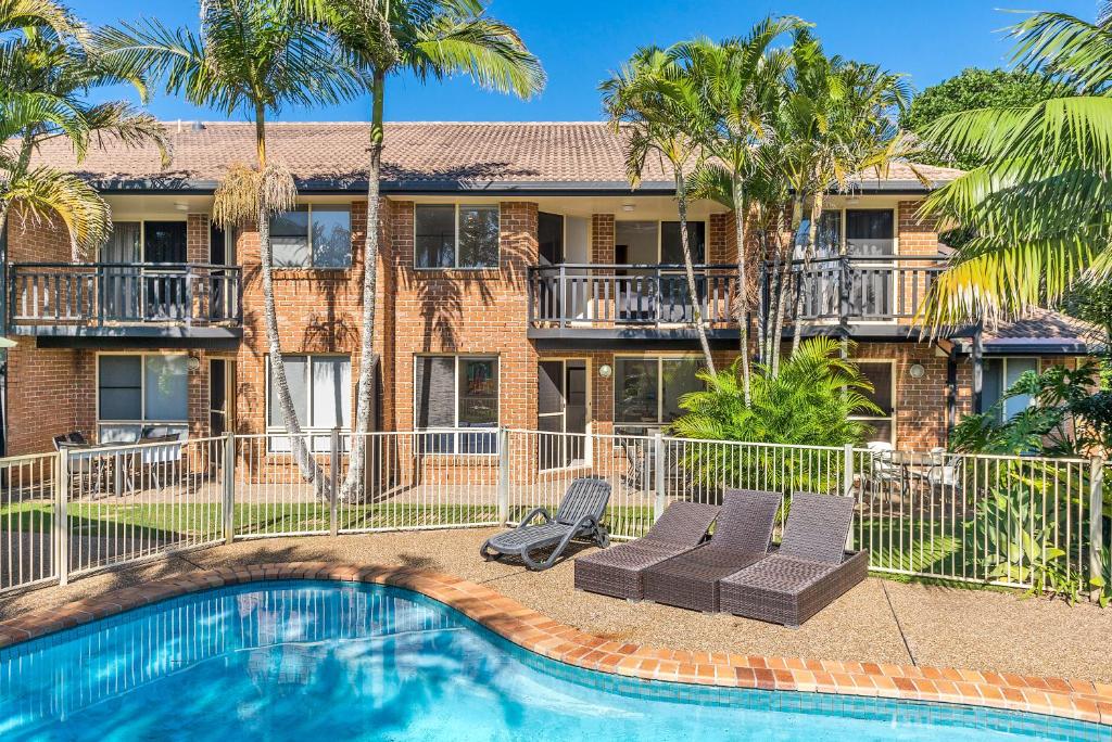 a swimming pool in front of a building with palm trees at Bayside Court Apartments in Byron Bay