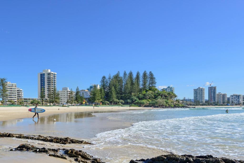 a person standing on the beach with a surfboard at Bayview Apartments Rainbow Bay in Gold Coast