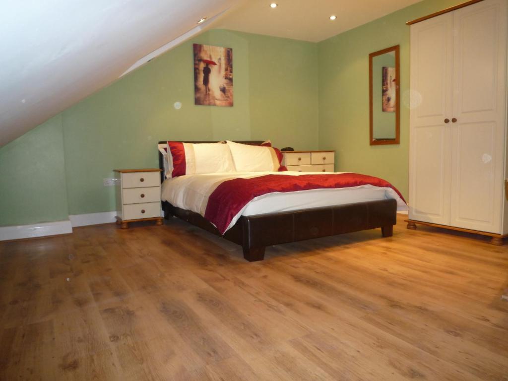 1 dormitorio con cama, paredes verdes y suelo de madera en Three Bedroom Flat, Camborne Avenue W13, en Londres