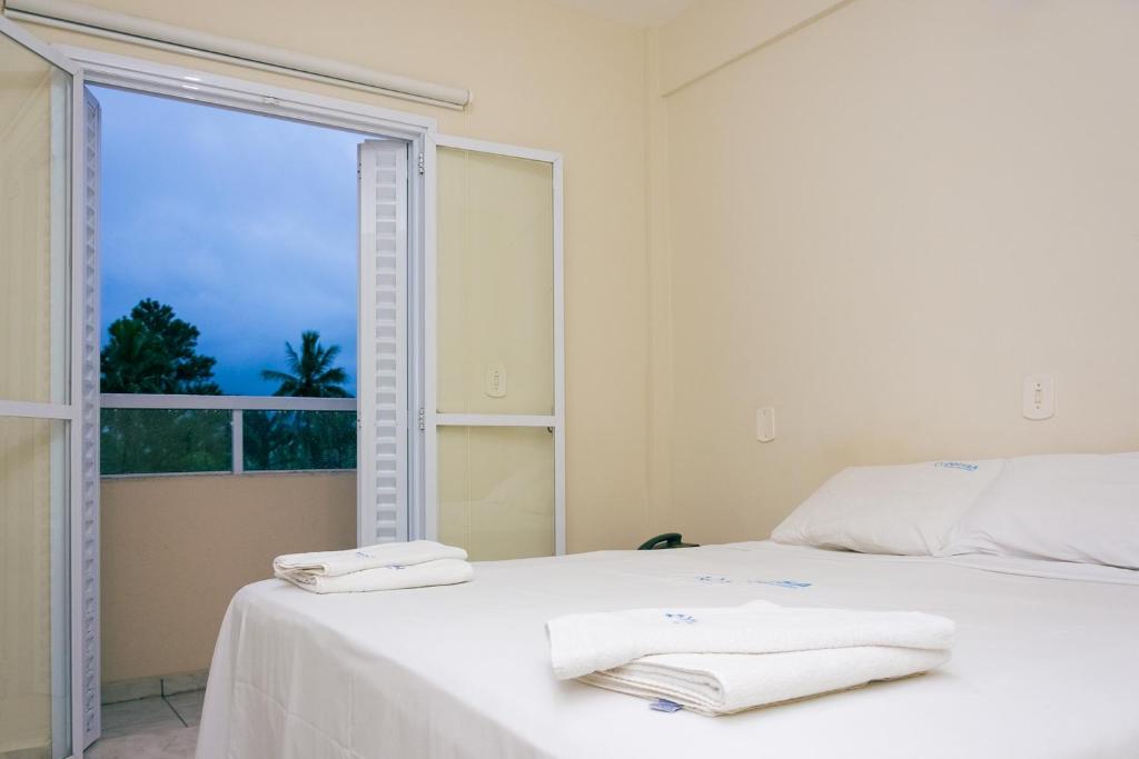 卡拉瓜塔圖巴的住宿－Pousada Jofisa Caraguá，一间白色卧室,配有窗户和床上的两条毛巾