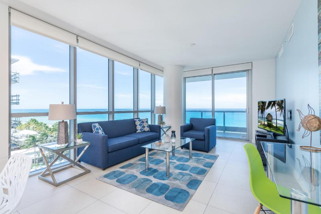Global Luxury Suites at Monte Carlo في ميامي بيتش: غرفة معيشة مع أثاث أزرق ونوافذ زجاجية