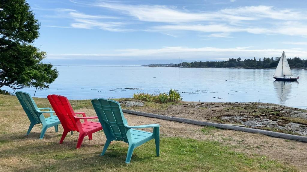3 Stühle neben einem Wasserkörper mit einem Segelboot in der Unterkunft Dae's Seaside Dream in Victoria