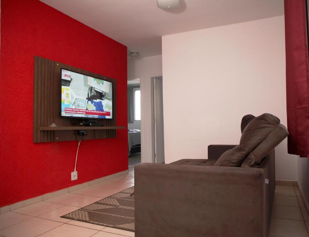 a living room with a couch and a tv on a red wall at Apartamento Aeroporto/ Uniube in Uberaba