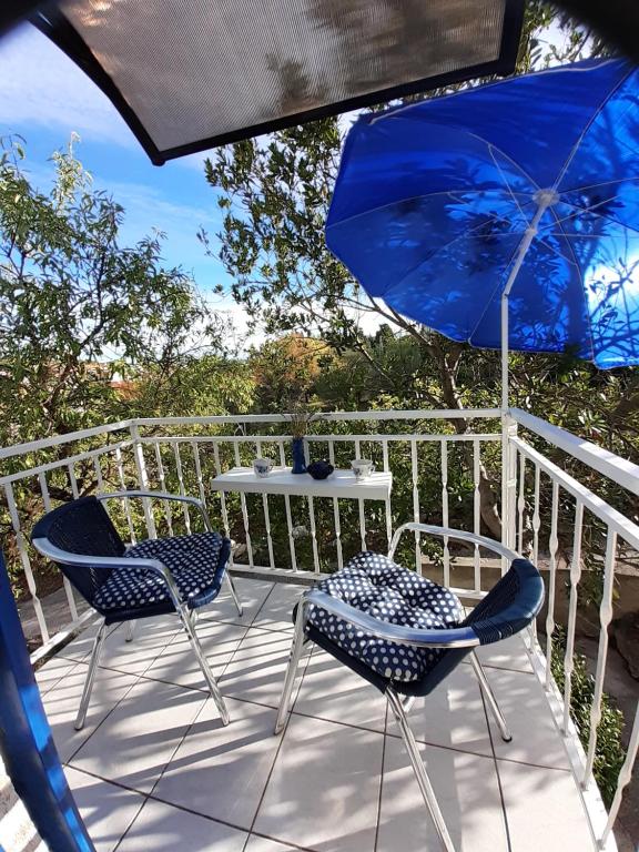 a patio with two chairs and a table with a blue umbrella at Apartment Diana in Prvić Šepurine