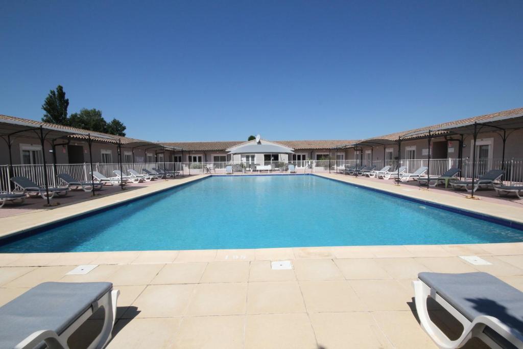 a large swimming pool with lounge chairs in a resort at Hôtel Saint Louis in Le Thor