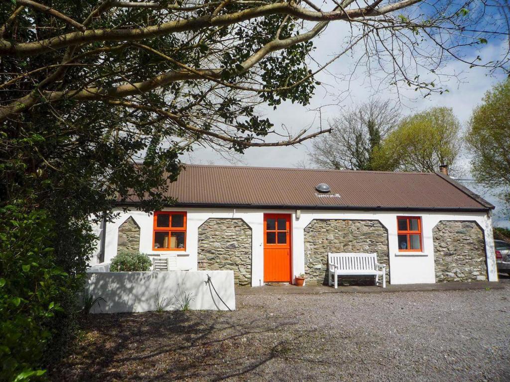 um edifício branco com uma porta laranja e um banco em Kizzie Cottage Killorglin by Trident Holiday Homes em Killorglin