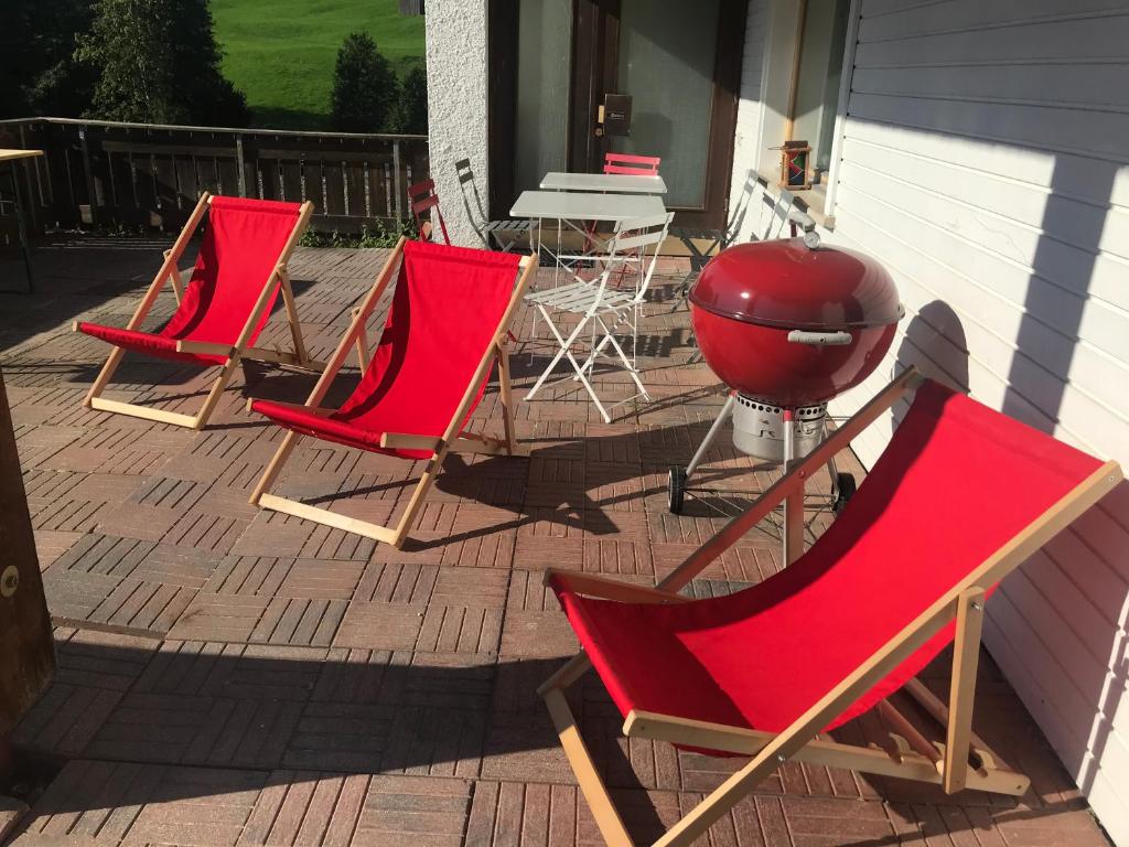 drie rode stoelen en een grill op een patio bij Kleine Ferienwohnung am Rande der Wildnis in Sibratsgfäll
