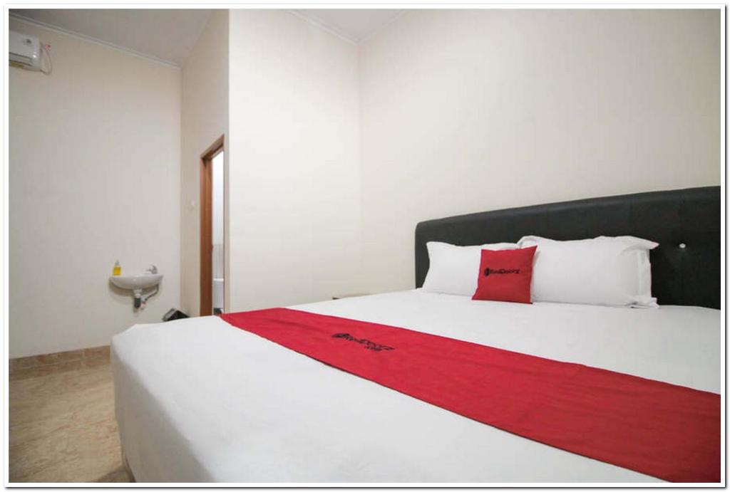 RedDoorz Syariah @ Jatinegara في جاكرتا: سرير أبيض كبير عليه بطانية حمراء