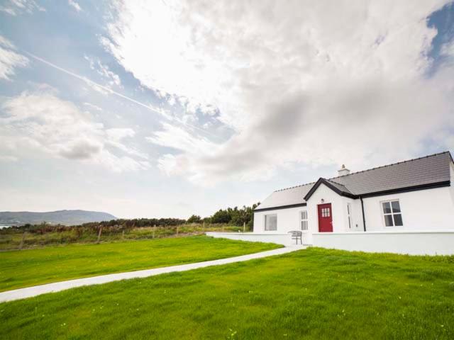 ein weißes Haus mit einer roten Tür und einem grünen Feld in der Unterkunft Barr an Uisce in Achill Sound