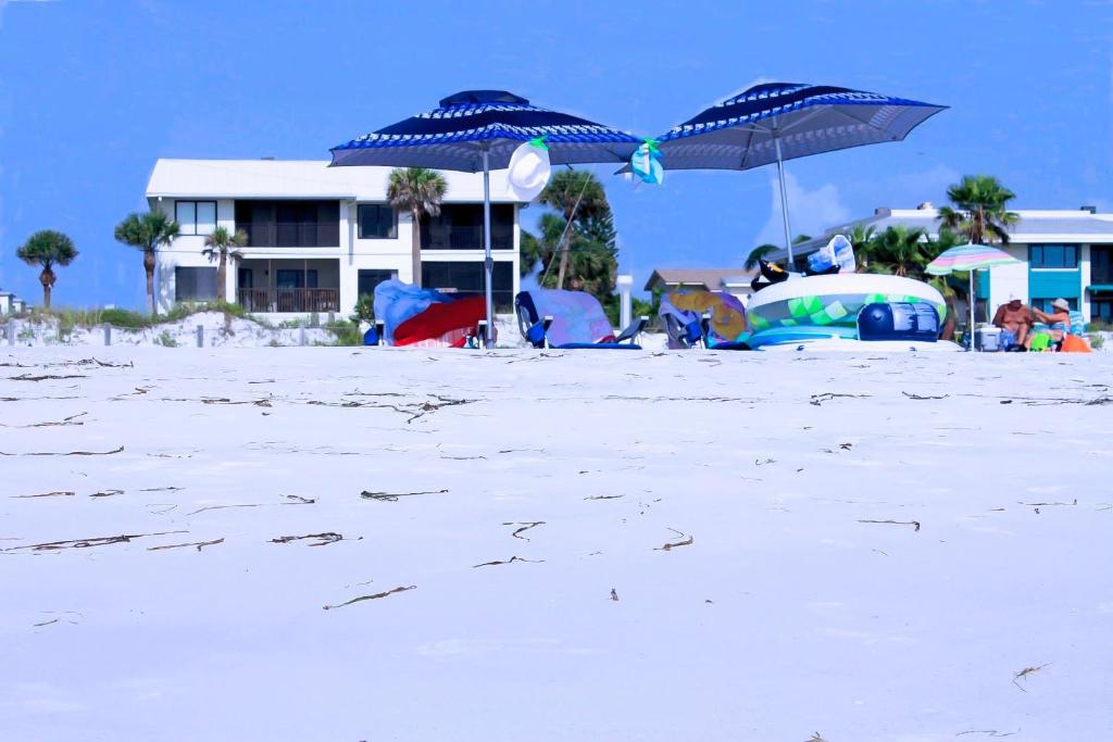 a beach with two blue umbrellas and a building at Anna Maria Island Beach Sands 101 in Bradenton Beach