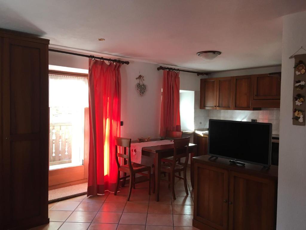 eine Küche mit roten Vorhängen, einem Tisch und einem TV in der Unterkunft LO PONTON cir 0022 in Introd