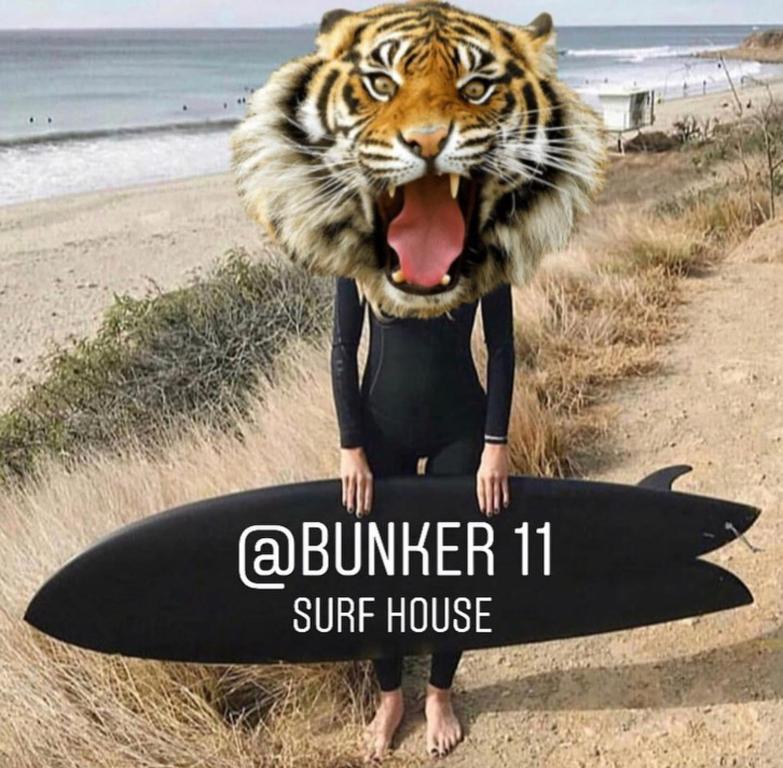 een vrouw in een nat pak met een surfplank bij Bunker 11 Surf House in Charneca