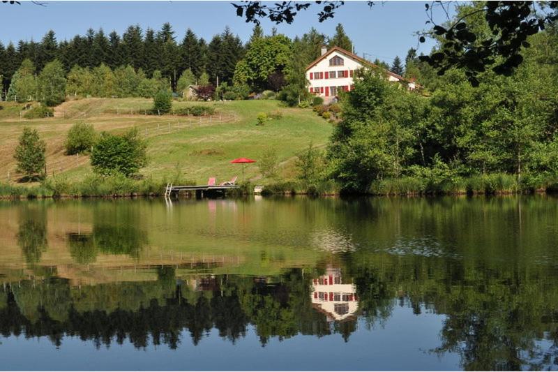 una casa sentada en una colina junto a un lago en "La Belle Chambre" dans une ferme avec etang privé dans la région des Mille Etangs Faucogney-et-La-Mer, en Écromagny