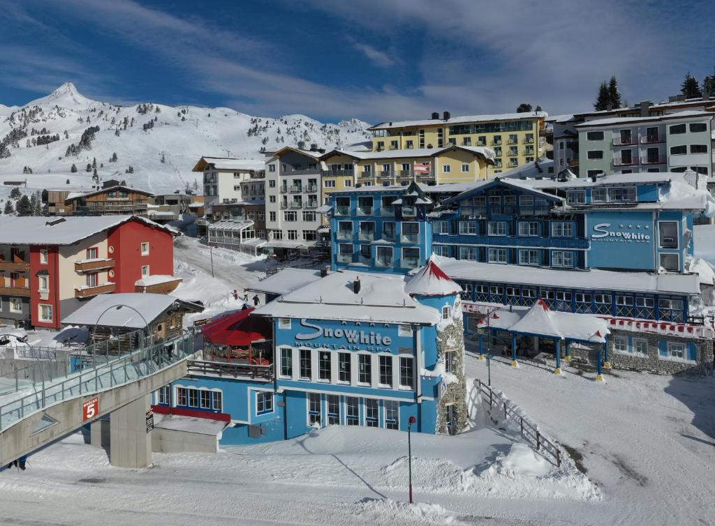 una ciudad con edificios cubiertos de nieve y una montaña en Sporthotel Snowwhite en Obertauern