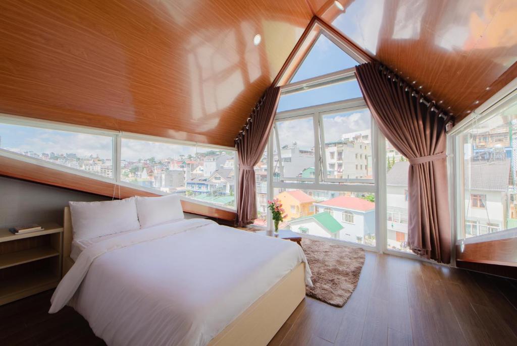 a bedroom with a white bed and large windows at Nắng Chiều Central Hotel in Da Lat