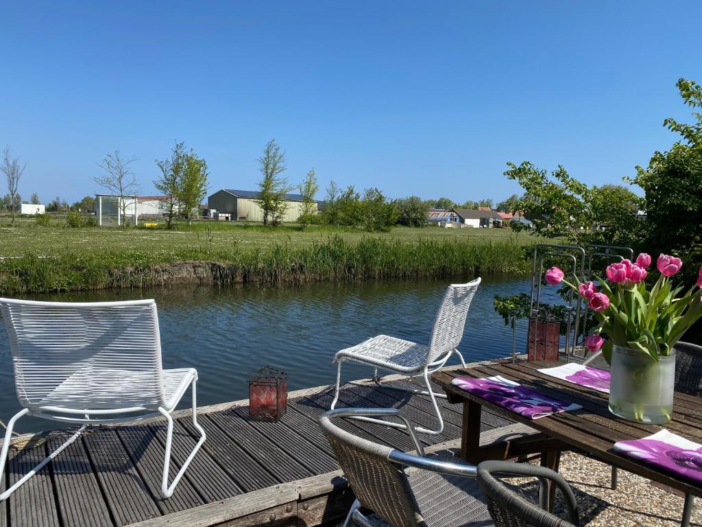 drie stoelen en een tafel op een terras naast het water bij Ferienpark Vislust Ferienhaus Balu mit eigenem Steiger zum angeln Ijsselmeer Niederlande in Wervershoof