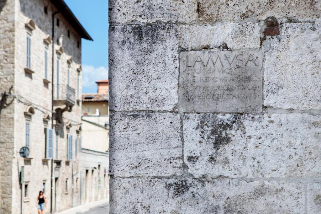 een vrouw die door een straat loopt naast een stenen muur bij Porta della Musa in Ascoli Piceno