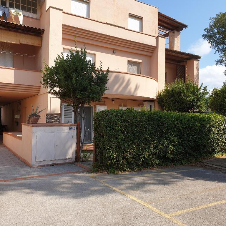 un bâtiment avec une haie en face d'un parking dans l'établissement Accogliente casa indipendente a 10 min dal mare, à Castiglione della Pescaia