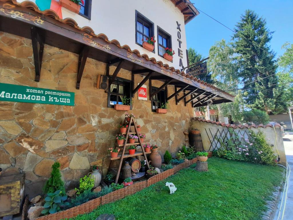 a building with a bunch of plants in a yard at Семеен хотел-ресторант Маламовата къща in Gotse Delchev