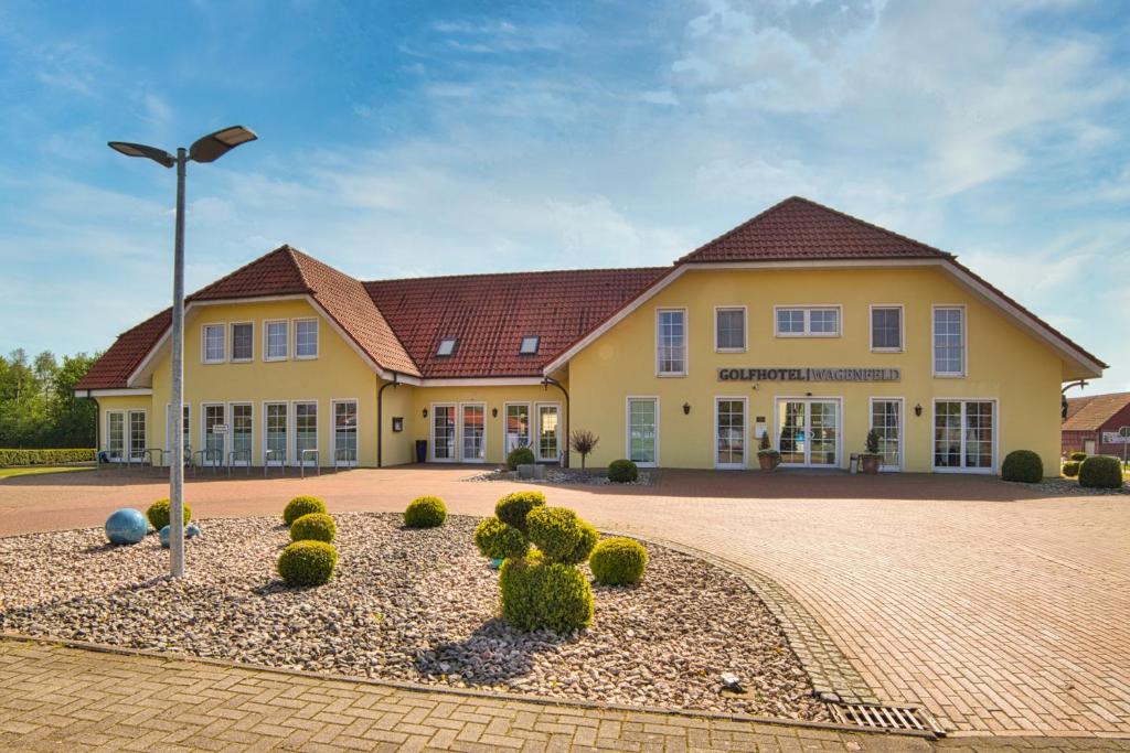 ein großes gelbes Gebäude mit Straßenbeleuchtung davor in der Unterkunft Golfhotel Wagenfeld in Wagenfeld