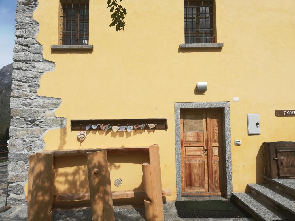 a yellow building with a wooden door and stairs at Rifugio Monte Zeus in Baceno